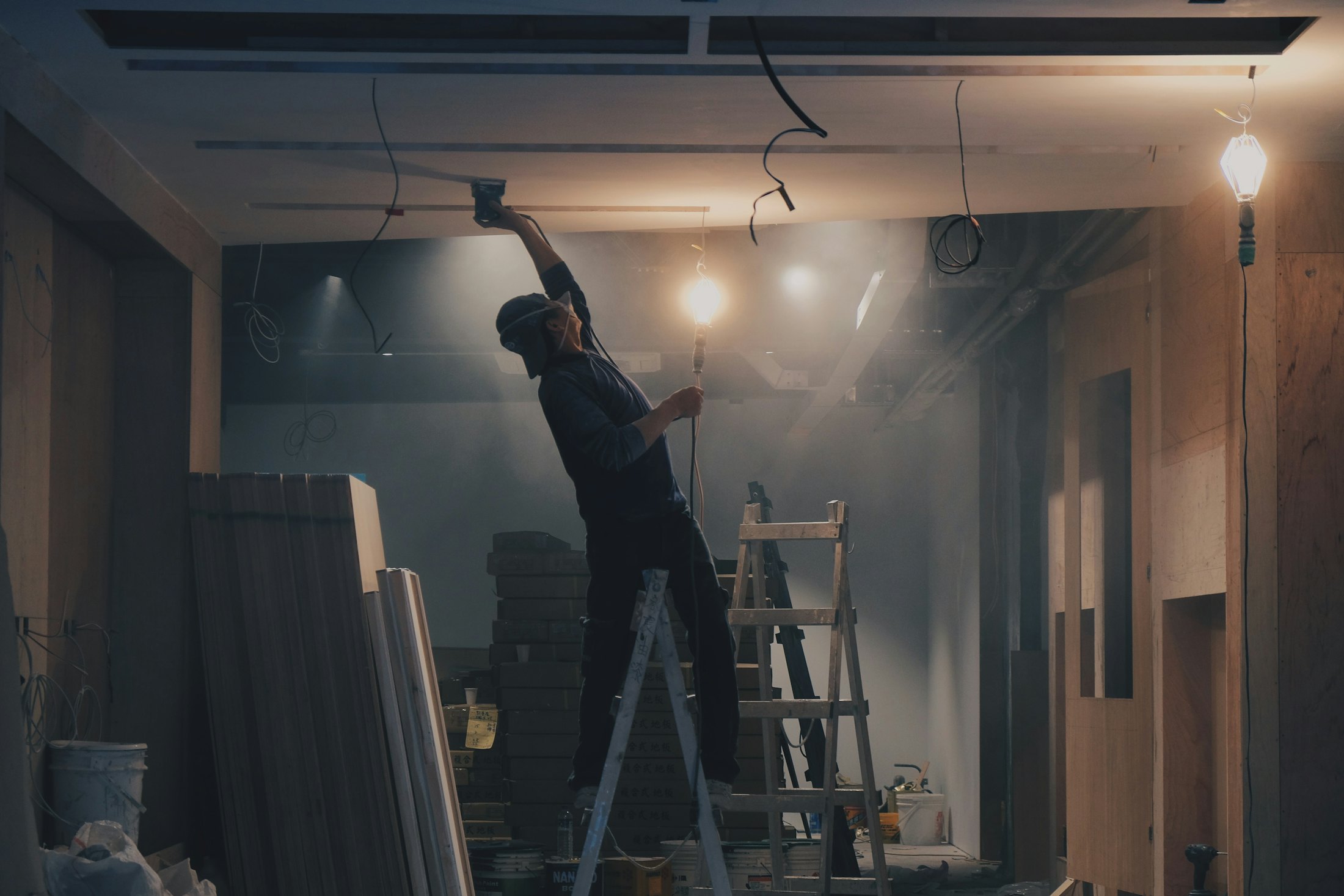 Drywaller working on a ceiling from a ladder in a room under construction